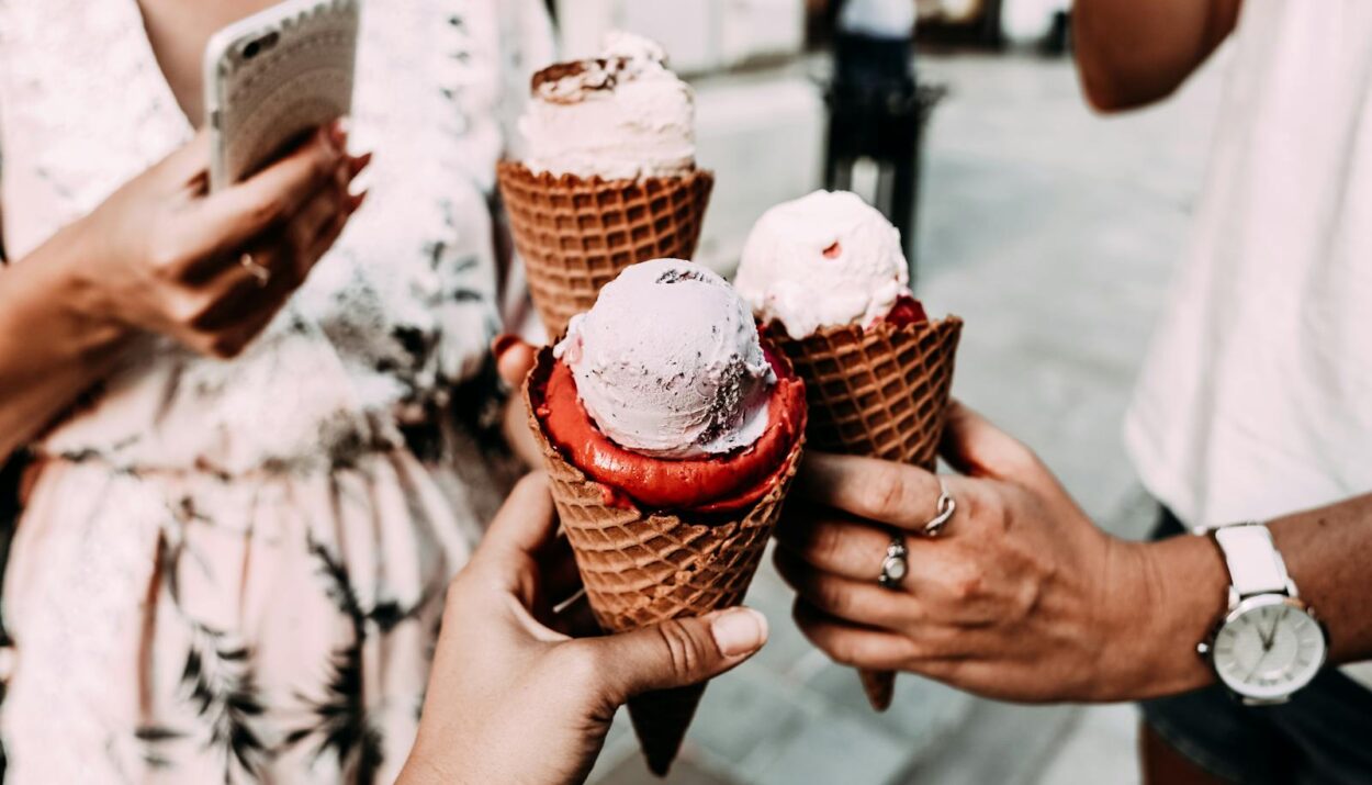 Crop anonymous friends in casual summer clothes clinking delicious cone ice creams while gathering on street