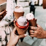 Crop anonymous friends in casual summer clothes clinking delicious cone ice creams while gathering on street